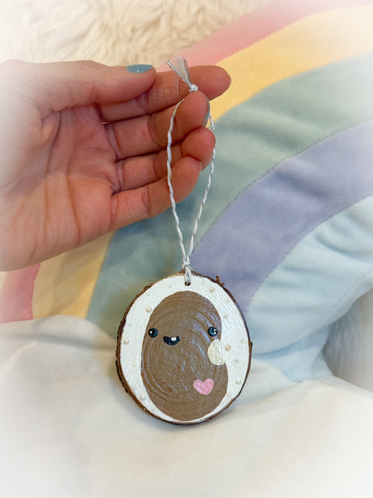 Hand holding a wooden ornament with a cute bean design against a soft, multicolored background.